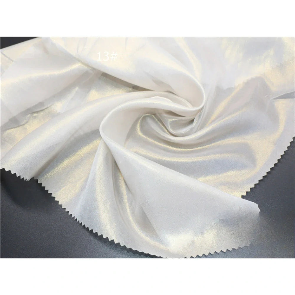 Un gros plan du tissu mousseline métallisé au mètre de Longan Craft France montre des plis brillants et irisés avec des bords en zigzag rosés ; "13#" est indiqué dans le coin supérieur gauche. Idéal pour la couture, ce tissu multicolore présente un éclat lumineux.