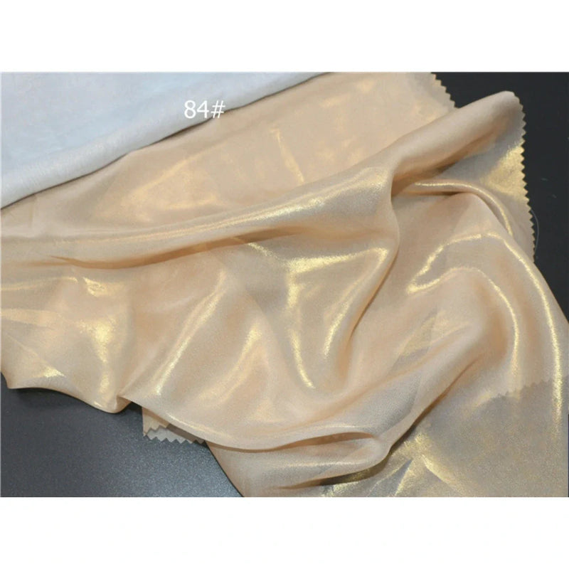 Un tissu mousseline beige clair métallisé au mètre par Longan Craft France, présentant une finition brillante et légèrement transparente, est présenté à côté d'un tissu blanc. Le numéro "84#" apparaît en texte blanc sur l'image.