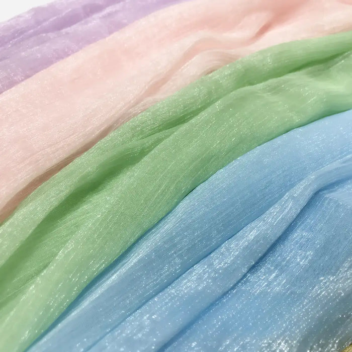 Les panneaux de Tissu mousseline plissé brillant au mètre de Longan Craft France dans les tons pastel de lavande, rose, vert et bleu présentent une texture lisse et une douce translucidité - un polyester transparent multicolore parfait de la collection Mousseline.