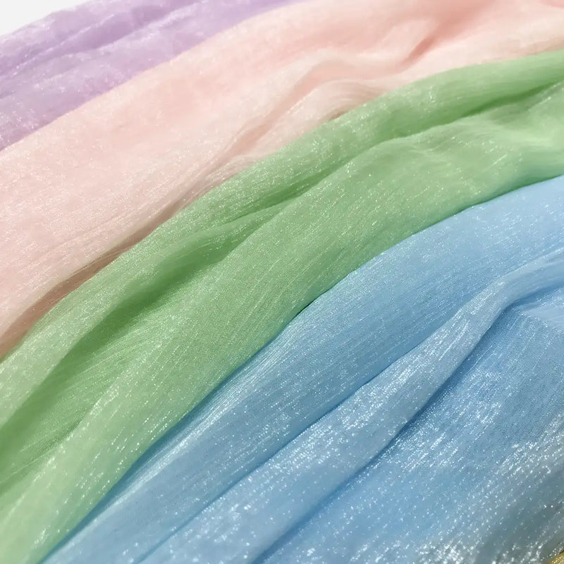 Les panneaux de Tissu mousseline plissé brillant au mètre de Longan Craft France dans les tons pastel de lavande, rose, vert et bleu présentent une texture lisse et une douce translucidité - un polyester transparent multicolore parfait de la collection Mousseline.