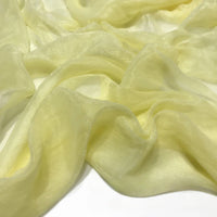 Gros plan sur le Tissu mousseline plissé brillant au mètre de Longan Craft France, un tissu polyester léger et brillant de couleur jaune, doucement drapé et rassemblé en plis fluides sur une surface blanche.