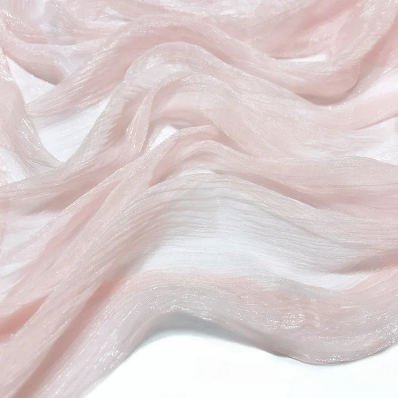 Gros plan sur le tissu mousseline plissé brillant au mètre de Longan Craft France, un polyester léger rose pâle au lustre subtil et aux plis ondulés, drapé délicatement sur un fond blanc.
