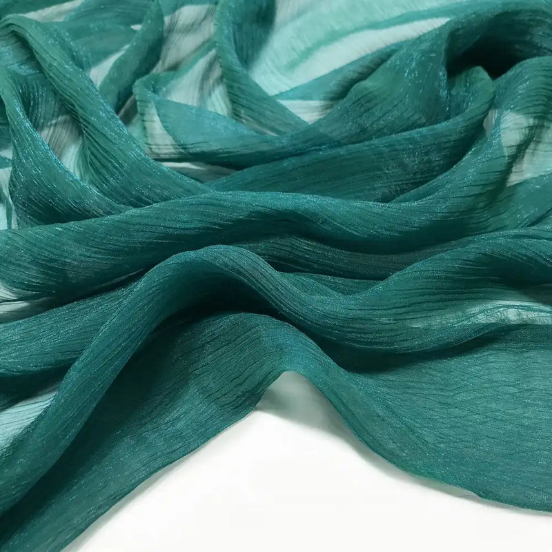 Gros plan sur la mousseline plissée brillant au mètre de Longan Craft France : un tissu léger et transparent en polyester de couleur vert sarcelle, avec une texture froissée et des plis doux et ondulés sur un fond blanc.