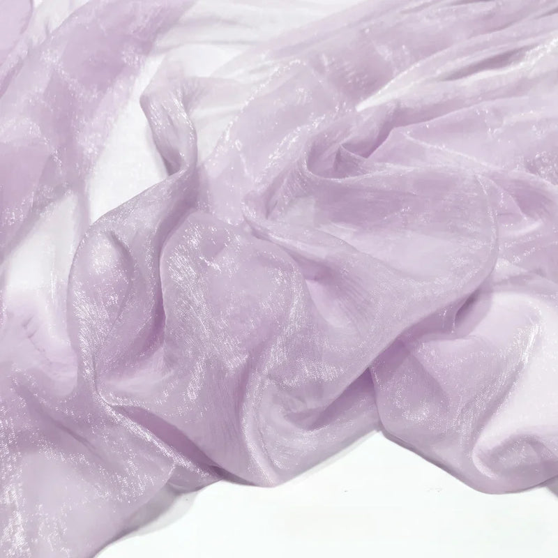 Gros plan sur le Tissu mousseline plissé brillant au mètre de Longan Craft France, un tissu léger, brillant et froissé en polyester drapé sur blanc, idéal pour les robes de soirée et similaire à l'organza lavande.