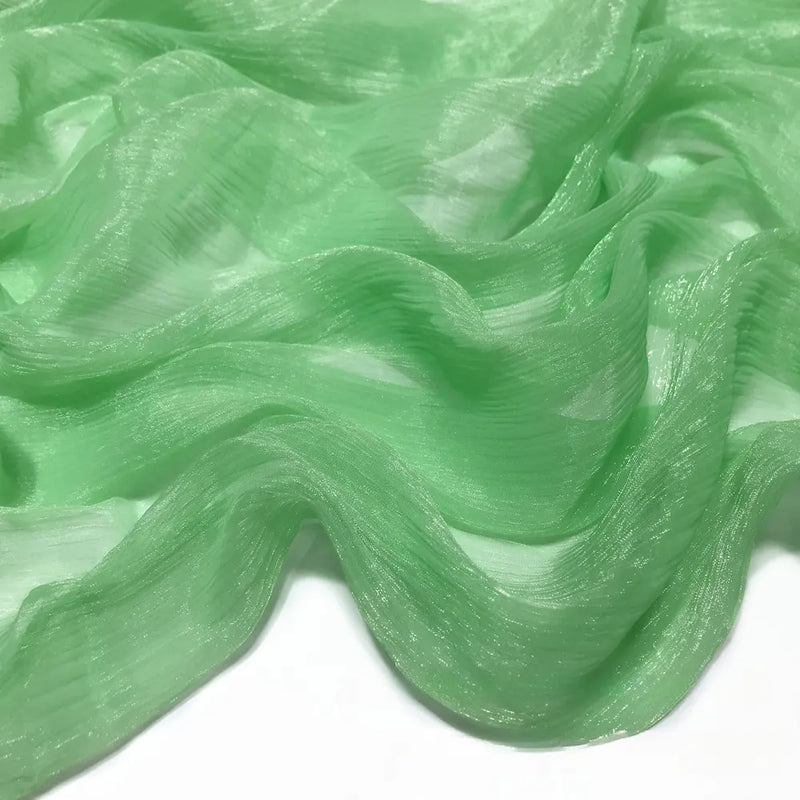 Gros plan sur un Tissu mousseline plissé brillant au mètre de Longan Craft France, de couleur vert clair et légèrement brillant, à la texture froissée et étalé sur une surface blanche.