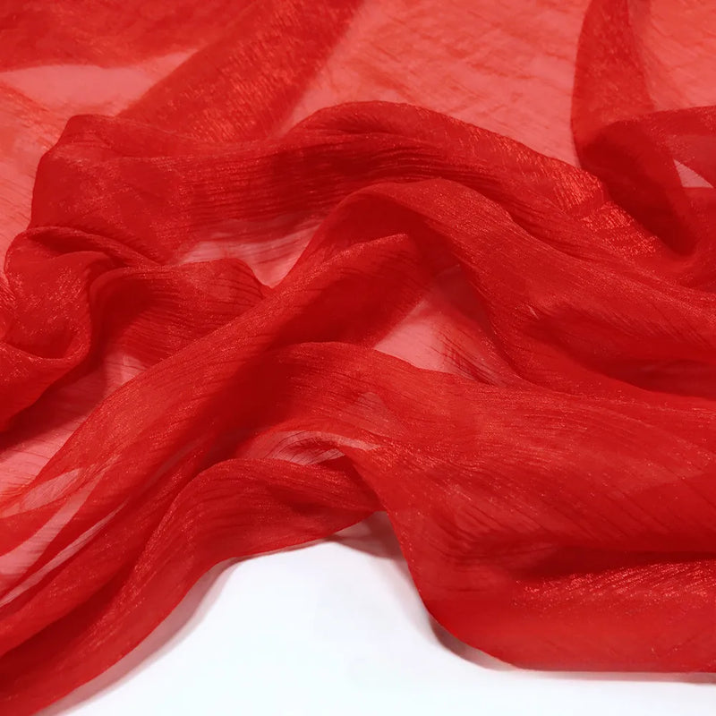 Gros plan sur le tissu de polyester plissé mousseline multicolore, transparent et léger de Longan Craft France, dont la texture subtilement froissée est drapée en plis souples sur une surface blanche.