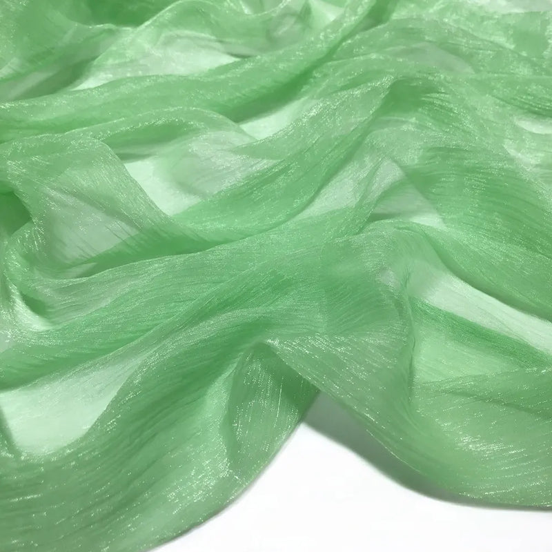 Gros plan sur le tissu mousseline plissé brillant semi-transparent vert clair de Longan Craft France, à la texture légèrement froissée et aux plis doux, disponible au mètre en polyester léger.