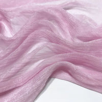 Gros plan sur le Tissu mousseline plissé brillant au mètre de Longan Craft France, une mousseline de polyester rose pâle, transparente et chatoyante, à la texture froissée, drapée en plis souples sur une surface blanche.