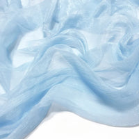 Le tissu mousseline plissé brillant bleu clair de Longan Craft France se drape librement sur une surface blanche, sa brillance subtile et sa texture translucide et aérienne mettant en valeur le tissu léger en polyester.