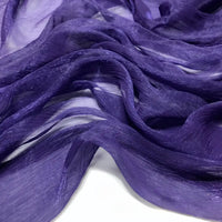 Gros plan sur le tissu mousseline plissé brillant au mètre de Longan Craft France dans un coloris violet profond, mettant en valeur ses plis légers, chatoyants et translucides sur une surface blanche. Cette mousseline de polyester froissée est douce et fluide.
