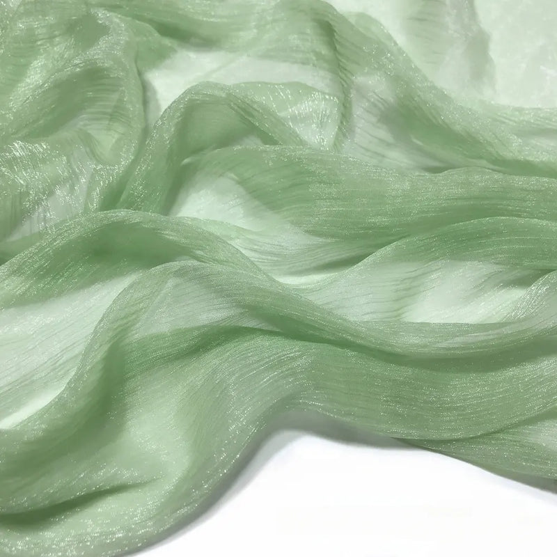 Gros plan sur le tissu mousseline plissé brillant au mètre vert clair de Longan Craft France, un polyester texturé transparent et légèrement brillant drapé sur un fond blanc.