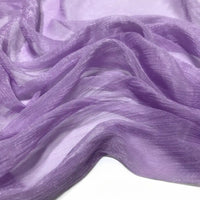 Gros plan sur le Tissu mousseline plissé brillant au mètre de Longan Craft France, un tissu de polyester transparent, léger et chatoyant dans les tons lavande, délicatement drapé en plis doux sur une surface blanche.
