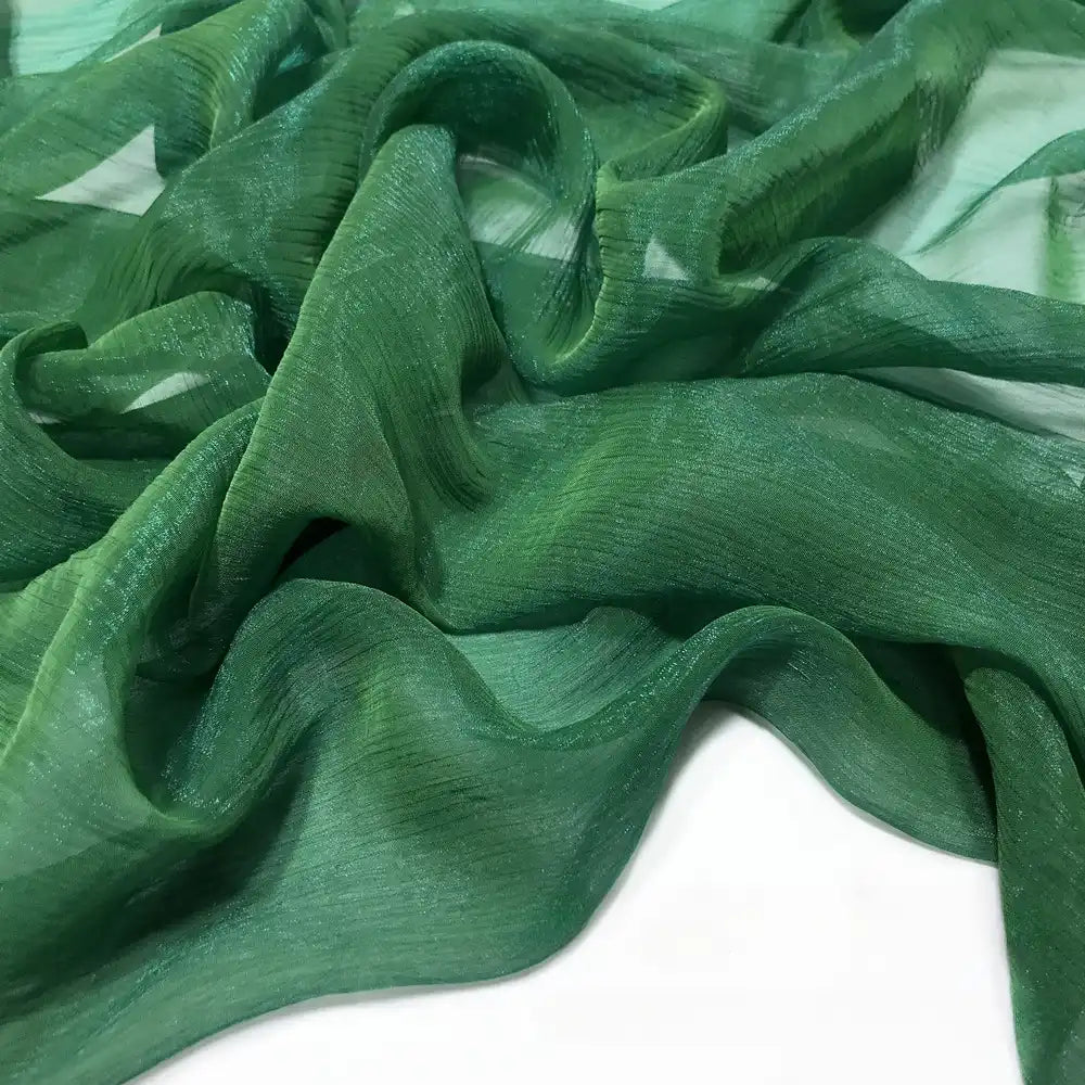 Gros plan sur le Tissu mousseline plissé brillant au mètre de Longan Craft France - une mousseline de polyester verte, transparente, légère et froissée - drapée sur une surface blanche plane.