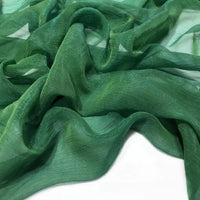 Gros plan sur le Tissu mousseline plissé brillant au mètre de Longan Craft France - une mousseline de polyester verte, transparente, légère et froissée - drapée sur une surface blanche plane.