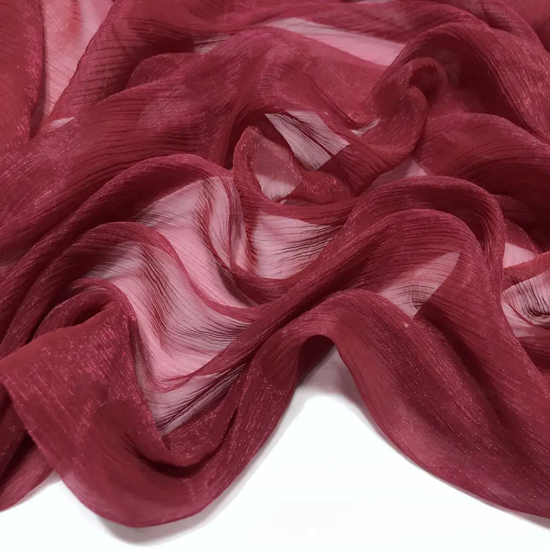 Gros plan sur le Tissu mousseline plissé brillant au mètre de Longan Craft France en marron, montrant ses plis ondulés, légers et transparents, gracieusement drapés sur une surface blanche.