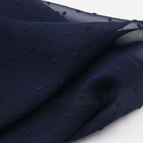 Un gros plan de Mousseline à plumetis au mètre de Longan Craft France révèle un tissu jacquard léger et diaphane dont la surface douce et légèrement transparente est parsemée de points multicolores délicatement en relief.