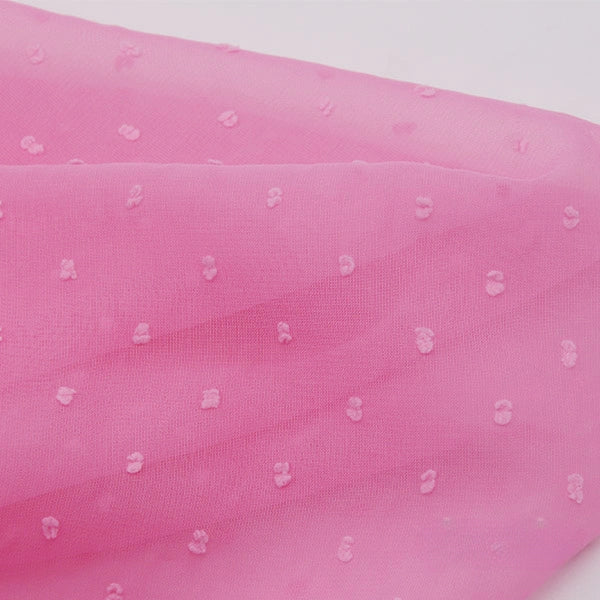 Un gros plan de la Mousseline à plumetis au mètre de Longan Craft France montre un tissu jacquard transparent et doux avec de fins points multicolores en relief, sur un fond blanc qui met en évidence sa qualité délicate et aérienne.