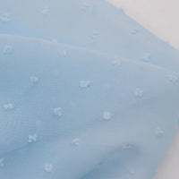 Un gros plan de Mousseline à plumetis au mètre de Longan Craft France montre son tissu jacquard bleu clair, doté d'une texture douce et de points brodés multicolores régulièrement espacés.