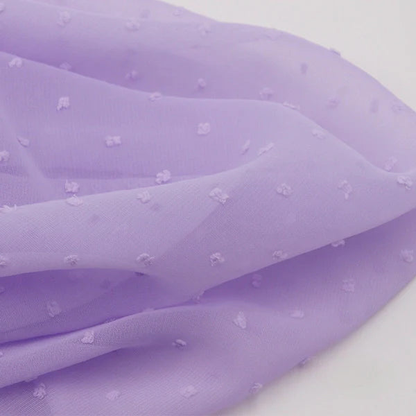 Gros plan sur Mousseline à plumetis au mètre de Longan Craft France : tissu jacquard mousseline doux avec de petits points texturés, délicatement drapé et plié sur une surface blanche.