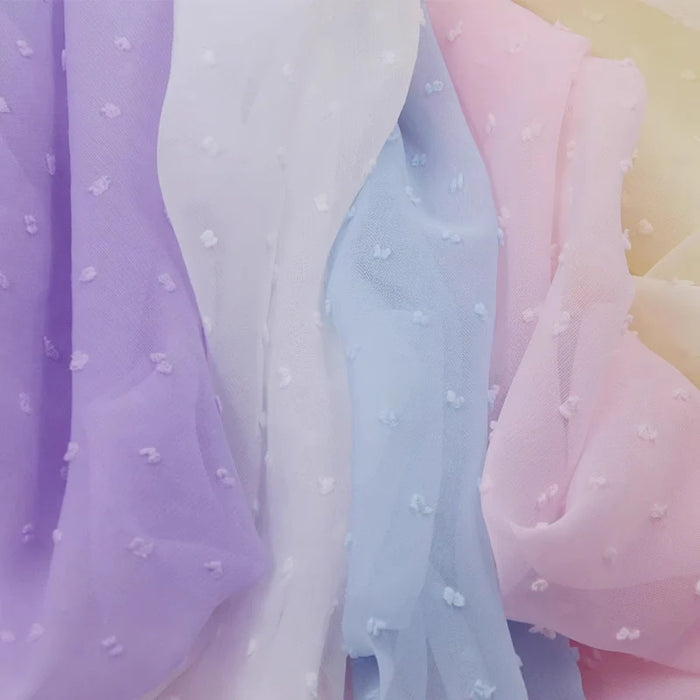 Gros plan sur Mousseline à plumetis au mètre de Longan Craft France - tissus mousseline jacquard doux dans les tons pastel de lavande, blanc, bleu, rose et jaune avec une texture de points en relief, qui se superposent délicatement.