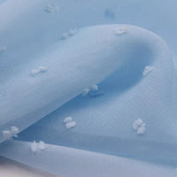 Gros plan sur Mousseline à plumetis au mètre de Longan Craft France : tissu jacquard doux avec des points brodés multicolores sur une surface en polyester bleu clair, légèrement translucide. Les plis doux ajoutent une profondeur élégante et ombragée.