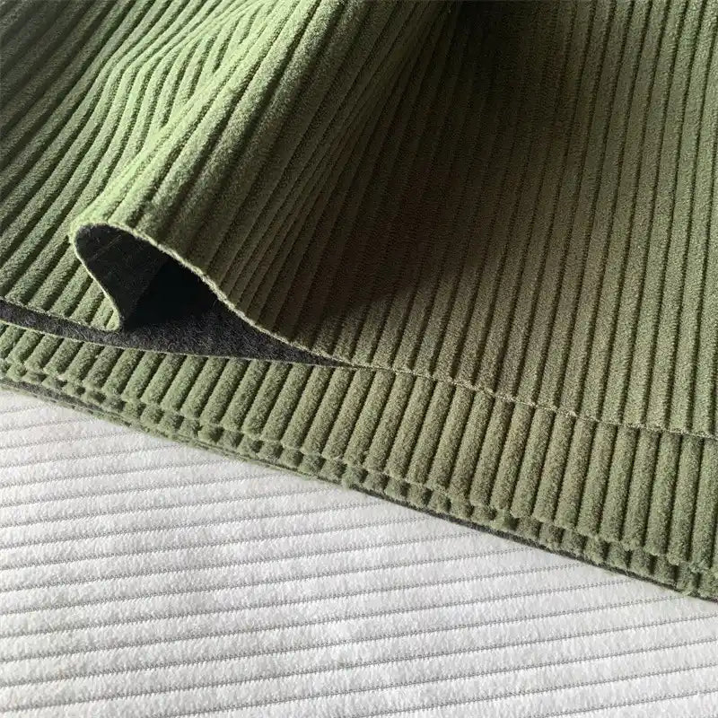 Gros plan sur le Tissu côtelé polyester 4,5 côtes au mètre de Longan Craft France en velours vert uni à côtes larges, drapé pour montrer les coutures nettes - idéal pour les pantalons ou la décoration intérieure.