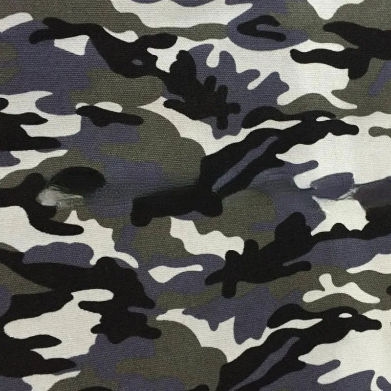 Un gros plan du tissu toile imprimé camouflage au mètre de Longan Craft France montre deux déchirures visibles dans le tissu polyester-coton, qui présente des nuances de noir, de gris et de blanc - idéal pour les vêtements, les sacs à main ou les tentes.