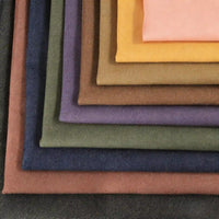 Une pile de pièces de denim colorées - marron, jaune, violet, vert, bleu et rose - fabriquées à partir de denim extensible Tissu 9,5 oz de Longan Craft France, parfait pour des jeans vibrants et confortables ou des projets créatifs.