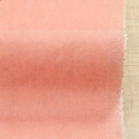 Gros plan sur le tissu Tissu denim extensible 9,5 oz de Longan Craft France - un tissu doux en coton-polyester de couleur pêche avec un tissage visible et des bords rosés, idéal pour les jeans - présenté sur une surface en bois clair.