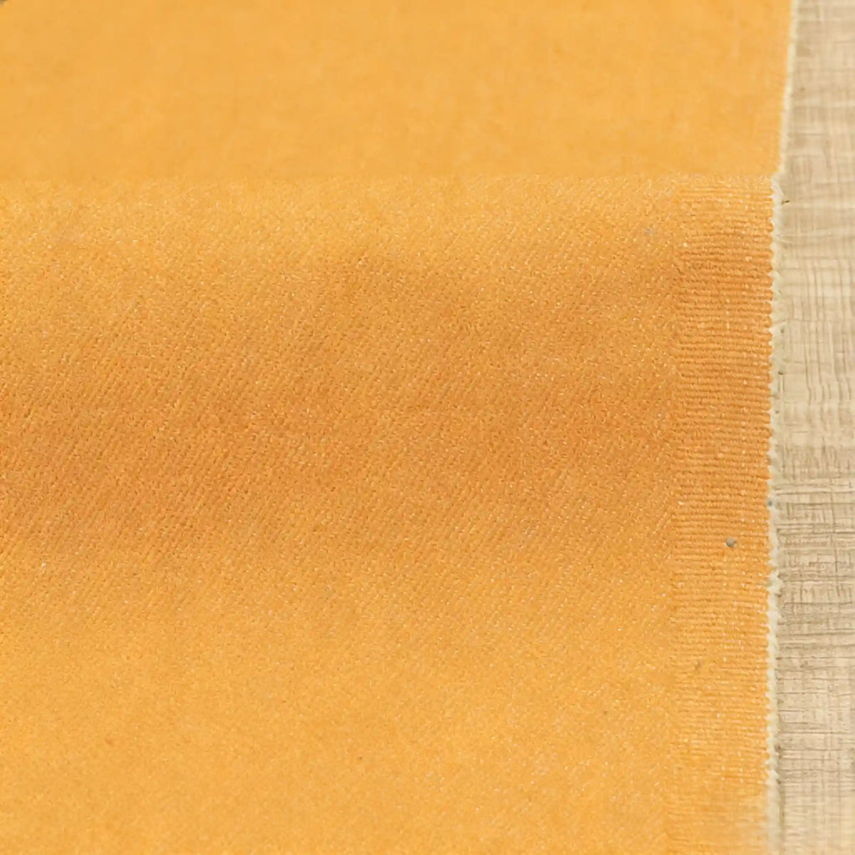 Gros plan sur le denim orange extensible 9,5 oz (coton-polyester) de Longan Craft France, montrant sa texture subtile et son bord effiloché, présenté sur une surface marron clair - tissu idéal pour les jeans au mètre.