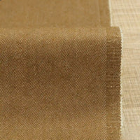 Un gros plan du Tissu denim extensible 9,5 oz au mètre de Longan Craft France montre son tissage lisse en coton-polyester idéal pour les jeans, contrastant avec la texture rugueuse de la toile de jute brune, le denim étant partiellement déroulé sur une surface plane.