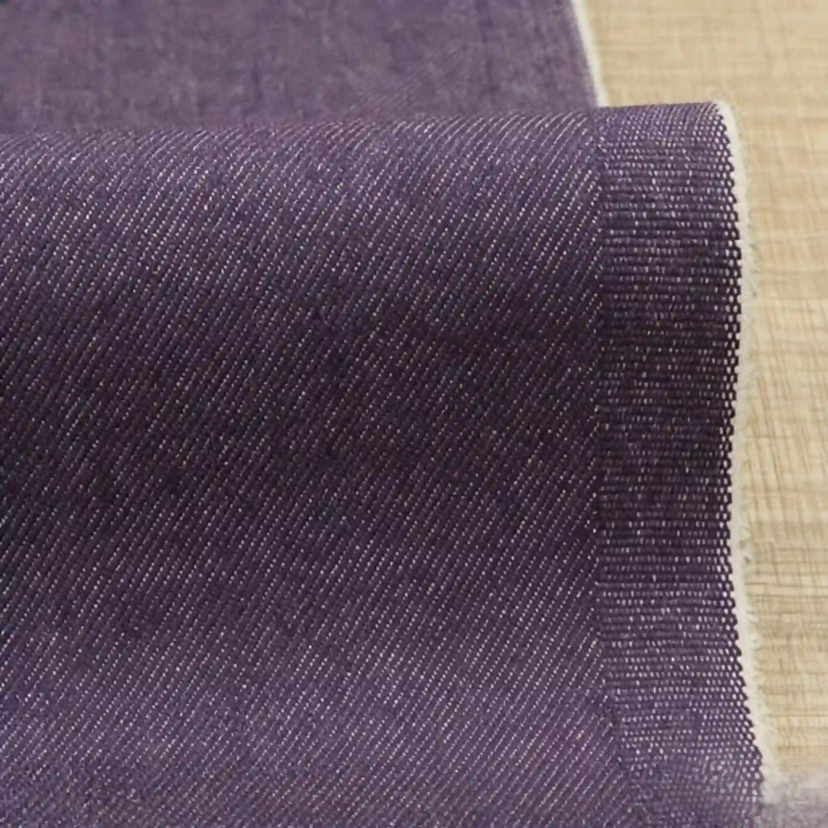 Un gros plan du denim Tissu extensible 9,5 oz au mètre de Longan Craft France montre le tissage diagonal fin, le bord de lisière texturé et la riche couleur pourpre ; ce denim extensible en coton-polyester est parfait pour la fabrication de jeans.