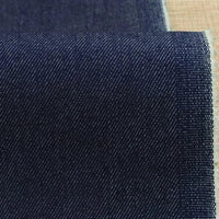 Gros plan sur le Tissu denim extensible 9,5 oz de Longan Craft France, coton-polyester bleu foncé avec motif sergé diagonal et lisière légèrement effilochée à droite. Fond en surface tissée marron.