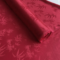 Une feuille enroulée de Tissu soie de mûrier et bambou imprimé jacquard au mètre de Longan Craft France, un tissu de doublure en soie et rayonne multicolore, doux et confortable, est présentée sur une surface plane.