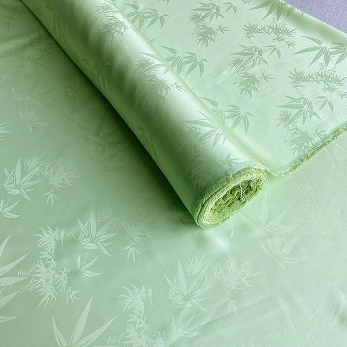 Un rouleau de Tissu soie de mûrier et bambou imprimé jacquard au mètre de Longan Craft France, un tissu de doublure en soie-rayon multicolore, lisse et doux, avec un subtil motif de feuilles, déroulé à plat pour mettre en valeur son design brillant.