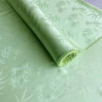 Un rouleau de Tissu soie de mûrier et bambou imprimé jacquard au mètre de Longan Craft France, un tissu de doublure en soie-rayon multicolore, lisse et doux, avec un subtil motif de feuilles, déroulé à plat pour mettre en valeur son design brillant.