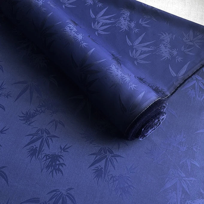 Un rouleau de Tissu soie de mûrier et bambou imprimé jacquard au mètre de Longan Craft France, présentant un motif de bambou multicolore, est partiellement déroulé pour révéler sa texture lisse et douce et sa finition brillante.