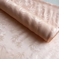 Un rouleau de Tissu soie de mûrier et bambou imprimé jacquard au mètre de Longan Craft France, un tissu de doublure doux et multicolore en soie-rayon avec un motif subtil de feuilles de bambou, est partiellement déroulé sur une surface plane.