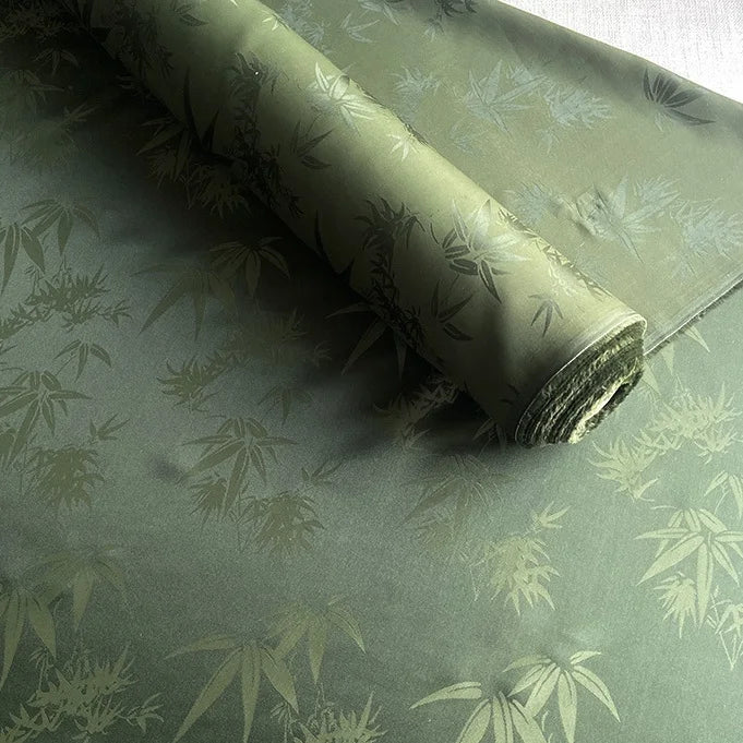 Un rouleau de Tissu soie de mûrier et bambou imprimé jacquard au mètre de Longan Craft France est partiellement déroulé, révélant son doux et confortable mélange de soie et de rayonne multicolore avec un motif complexe de bambou.