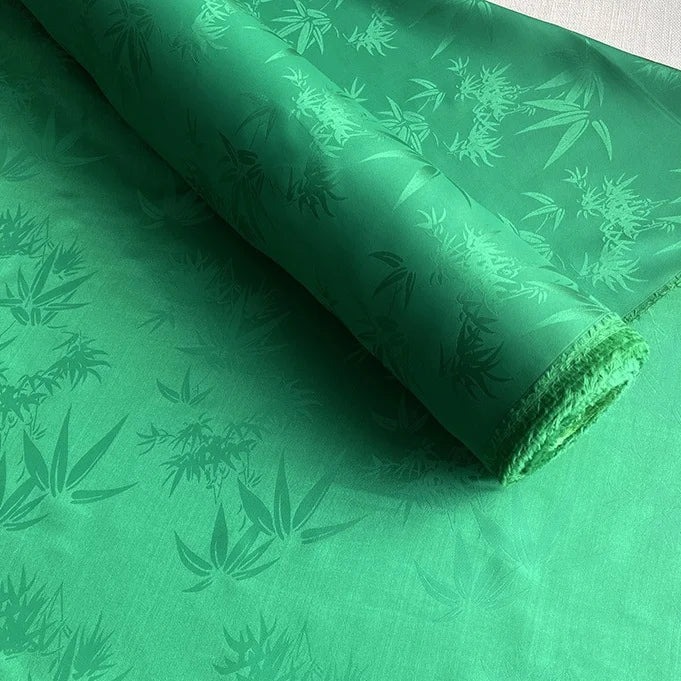 Une feuille partiellement déroulée du Tissu soie de mûrier et bambou imprimé jacquard au mètre de Longan Craft France, un tissu de doublure doux et confortable en soie et rayonne multicolore avec un élégant motif de feuilles de bambou.