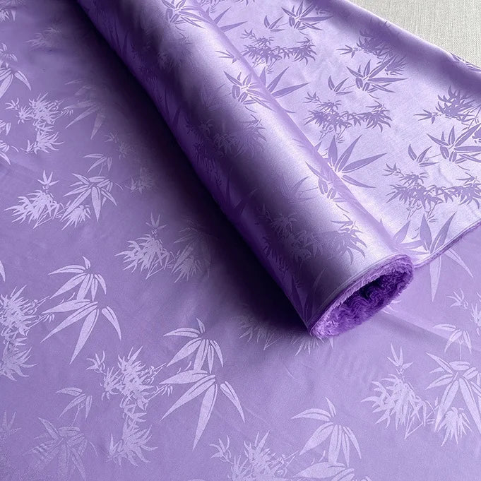 Un rouleau de Tissu soie de mûrier et bambou imprimé jacquard au mètre de Longan Craft France, un tissu de doublure en soie et rayonne multicolore, doux et confortable, est déroulé pour montrer sa texture lisse et son motif botanique détaillé ton sur ton.