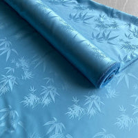 Un rouleau de Tissu soie de mûrier et bambou imprimé jacquard au mètre de Longan Craft France, au lustre doux et à la texture lisse, est partiellement déroulé, mettant en valeur une élégante doublure en soie-rayon multicolore.