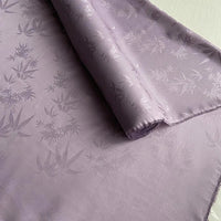 Un gros plan du tissu soie de mûrier et bambou imprimé jacquard au mètre de Longan Craft France montre son mélange de soie-rayon à motifs de feuilles, doux et brillant, partiellement déroulé et idéal comme tissu de doublure confortable.
