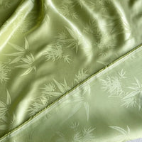 Gros plan sur le tissu soie de mûrier et bambou imprimé jacquard de Longan Craft France : tissu de doublure en soie-rayon vert clair au lustre subtil, au délicat motif de feuille de bambou et aux bords finis et non finis.