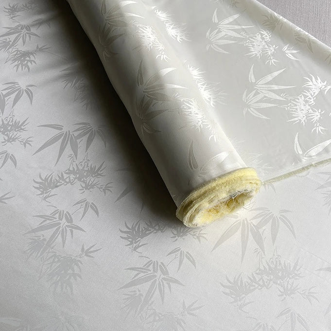 Un rouleau de tissu soie de mûrier et bambou imprimé jacquard au mètre de Longan Craft France, un tissu de doublure en soie et rayonne multicolore, doux et confortable, avec un léger éclat et une texture délicate, est partiellement déroulé sur une surface plane.