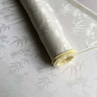 Un rouleau de tissu soie de mûrier et bambou imprimé jacquard au mètre de Longan Craft France, un tissu de doublure en soie et rayonne multicolore, doux et confortable, avec un léger éclat et une texture délicate, est partiellement déroulé sur une surface plane.