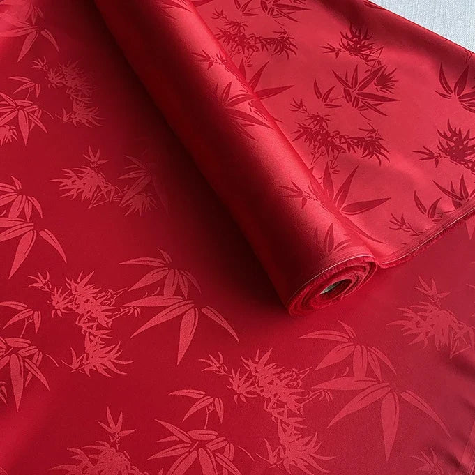 Un rouleau de Longan Craft France tissu soie de mûrier et bambou imprimé jacquard au mètre, présentant un motif brillant de feuilles de bambou, déroulé sur une surface plane. Ce tissu de doublure en soie et rayonne multicolore est doux et confortable.