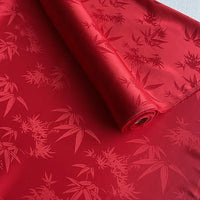 Un rouleau de Longan Craft France tissu soie de mûrier et bambou imprimé jacquard au mètre, présentant un motif brillant de feuilles de bambou, déroulé sur une surface plane. Ce tissu de doublure en soie et rayonne multicolore est doux et confortable.