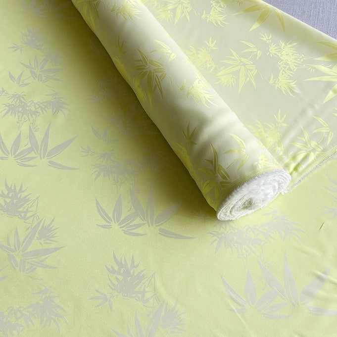 Un rouleau de tissu multicolore en soie de mûrier et bambou imprimé jacquard de Longan Craft France est partiellement déroulé, montrant sa texture lisse, son toucher doux et son subtil motif botanique. Vendu au mètre pour les doublures ou l'artisanat.