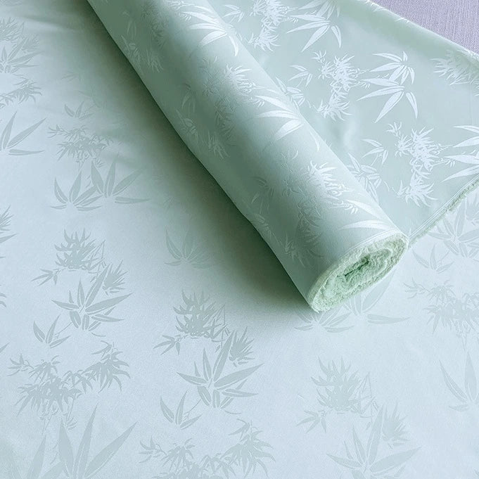 Un rouleau de Tissu soie de mûrier et bambou imprimé jacquard au mètre de Longan Craft France est partiellement déroulé, montrant son tissu lisse et multicolore en soie et rayonne avec un motif décoratif subtil.